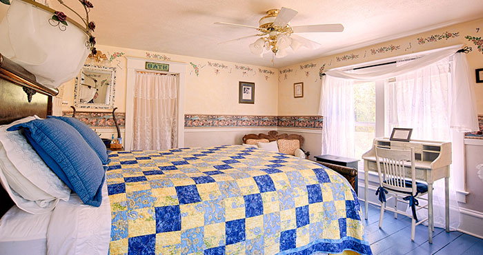 Quaint bedroom with blue quilt and desk.