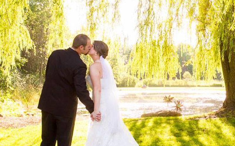 Bride and groom kissing under willow tree.